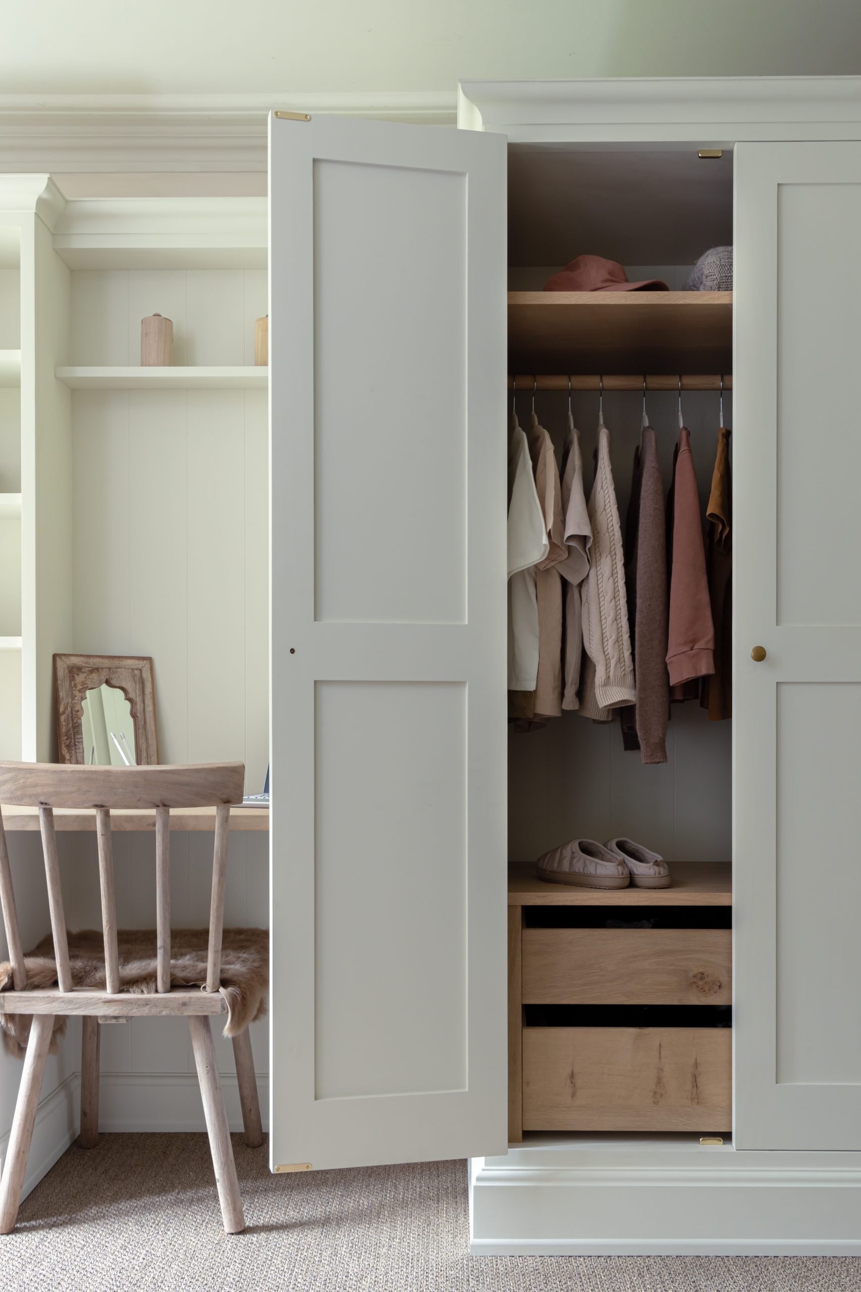 Open wardrobe with neatly arranged clothes and wooden drawers beside home desk