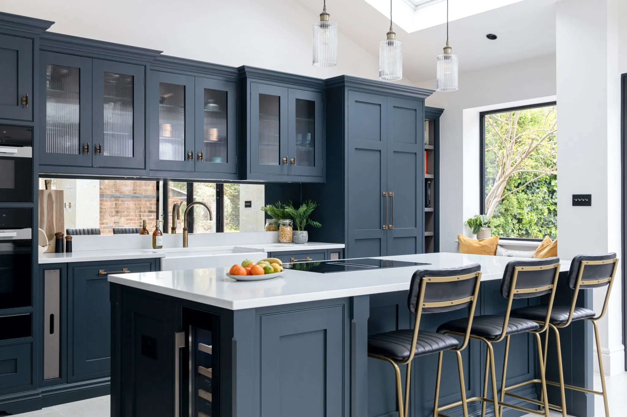 Oblique angle down navy cabinetry toward island; Lucca quartz counters, antique mirror splashback and bronze handles in focus
